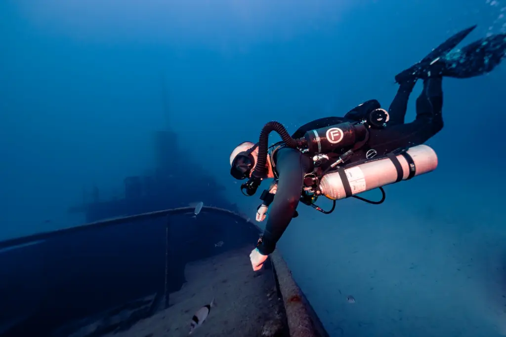 Diver holding the rusty railing of a sunken vessel in Malta