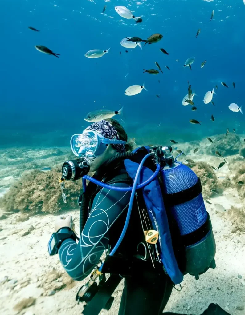 Diver surrounded by a school of fish on Malta's sandy seabed
