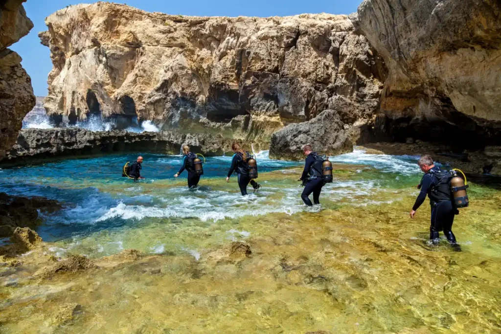 Group of divers entering the water from a rocky cove in Malta