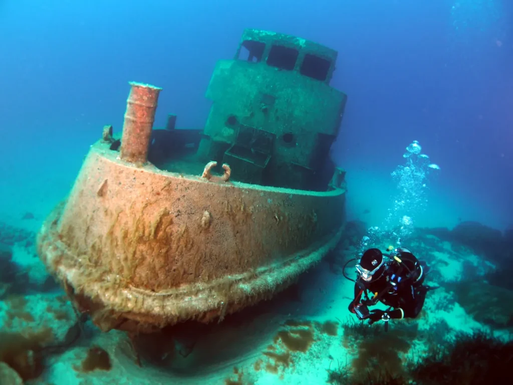 Diver swimming alongside a sunken tugboat wreck in Malta