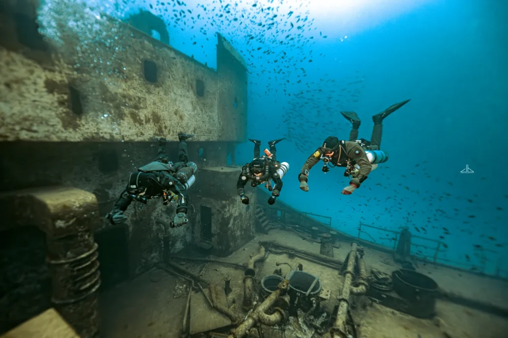Three divers exploring the deck of a WWII shipwreck in Malta